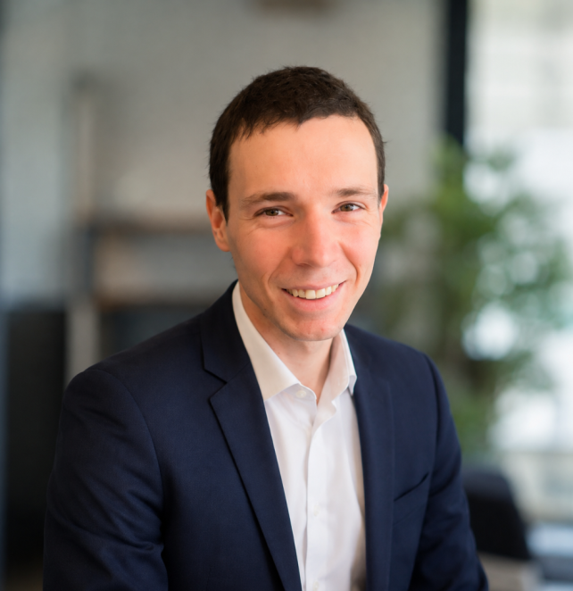 Professional headshot of a construction cost consultant wearing a suit, neutral office background, soft natural light, confident friendly expression, high quality photo